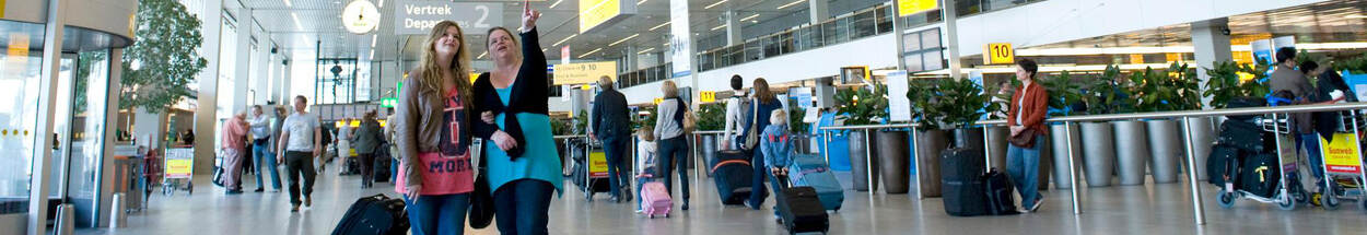 2 vrouwen bekijken bord met vluchtinformatie bij vertrekhal Schiphol