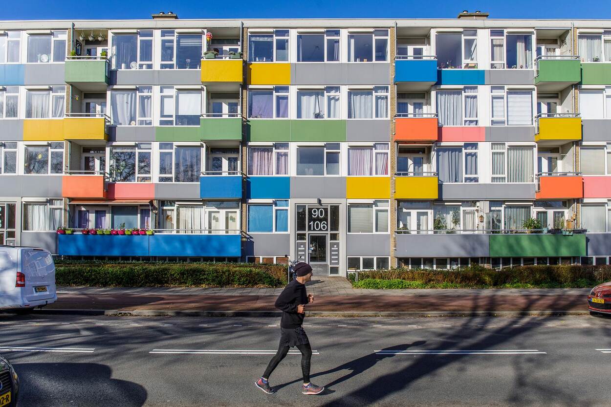 Een flatgebouw met kleurrijke balkonnetjes. Op de voorgrond rent een hardloper.