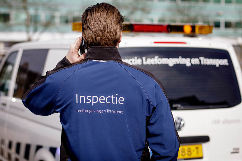 Een inspecteur staat bellend voor een inspectie bus.