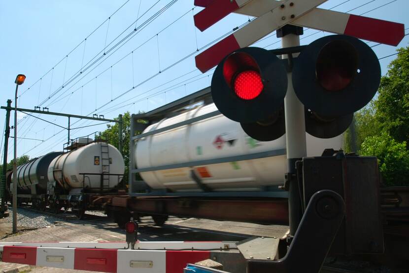 Spoorwegovergang met gesloten spoorbomen omdat een trein met tankwagons langskomt.
