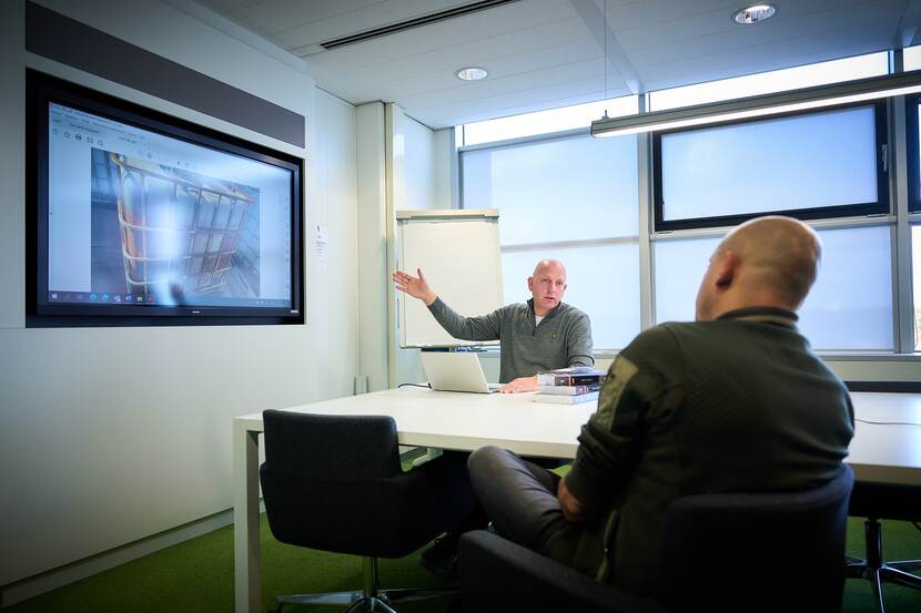Sean Beukers zit in een vergaderzaal op kantoor met een collega. Samen kijken ze op een scherm naar een foto van een IBC.