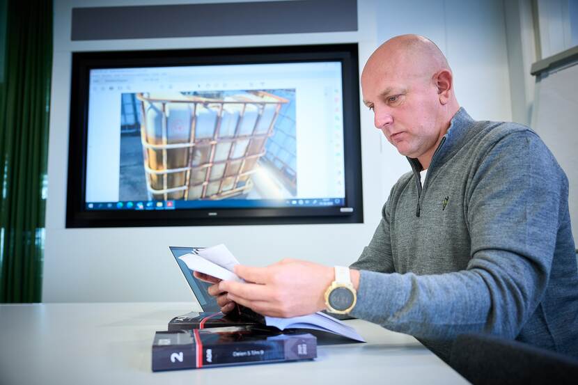 Sean Beukers zit op kantoor en neemt een aantal papieren door. Op de achtergrond staat op een scherm een foto van een IBC.
