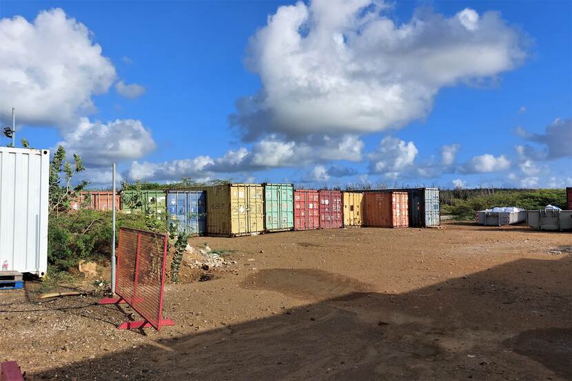 Een rij kleurrijke zeecontainers en vuilnisbakken.