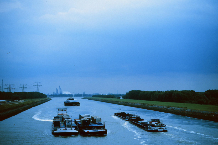 Overzichtsfoto van drie binnenvaartschepen die varen op water in een polderlandschap